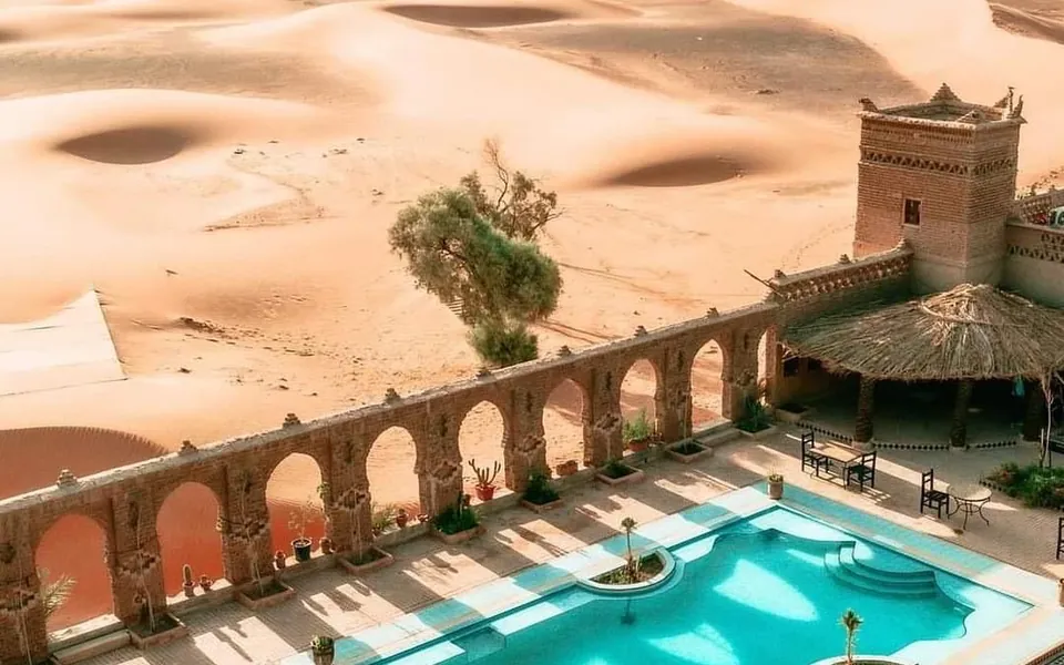 Hotel con piscina turquesa y arcos entre las dunas de Merzouga
