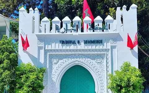 Puerta turquesa con arco de herradura en una fachada blanca almenada